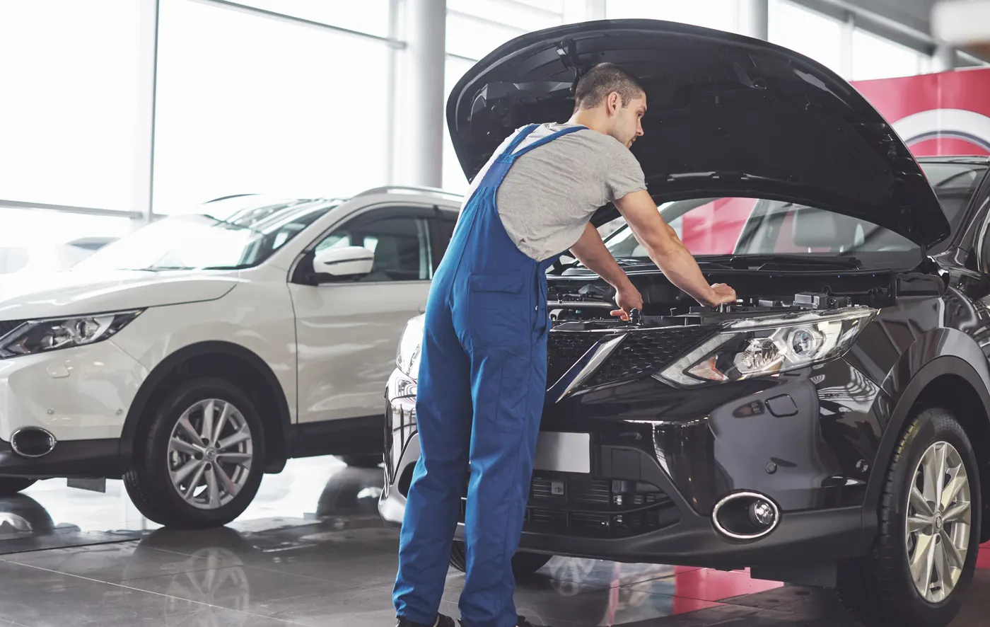 A mechanic in blue overalls working under the hood of a car